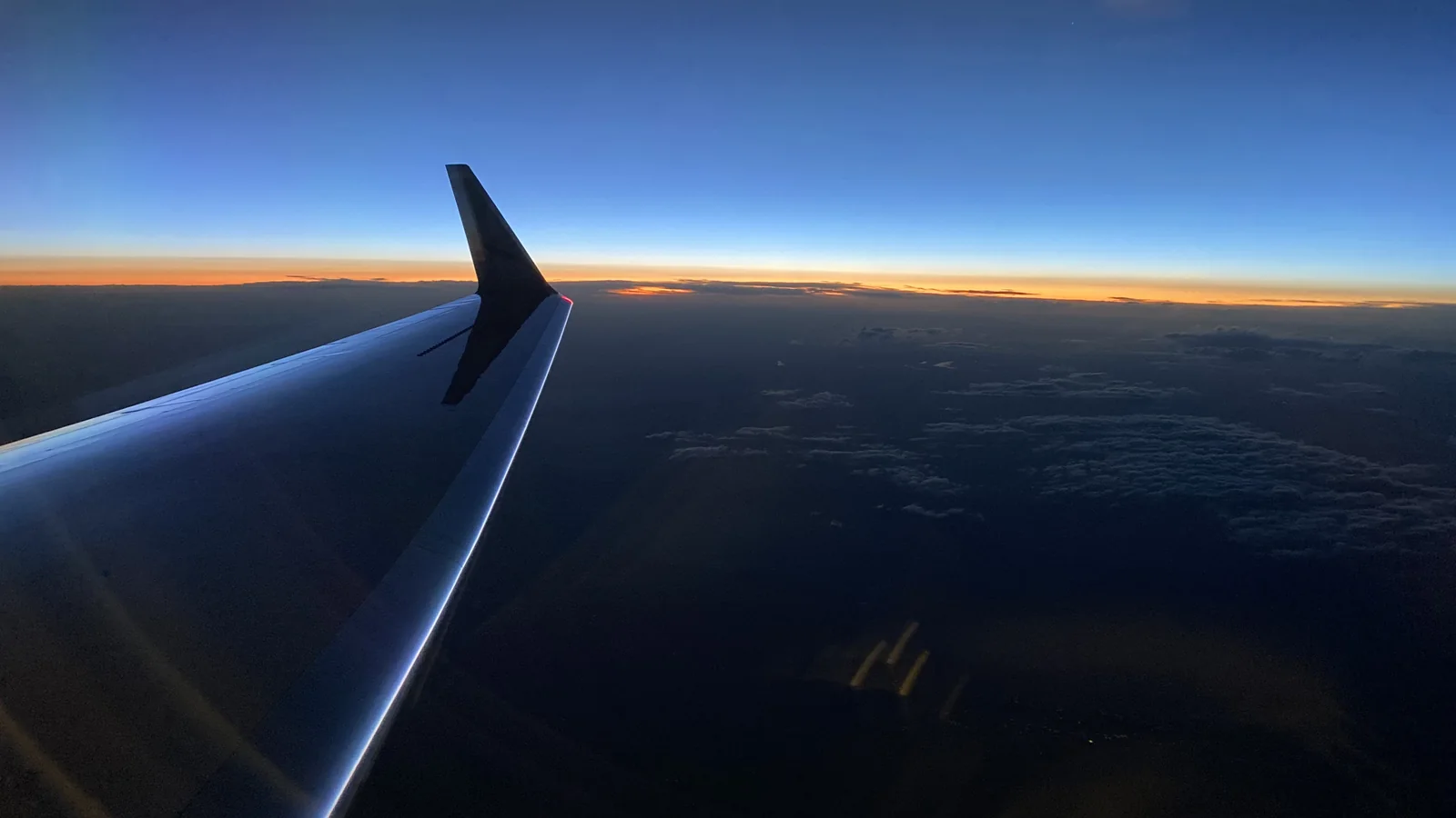 Aircraft wing silhouetted against a sunset above the clouds